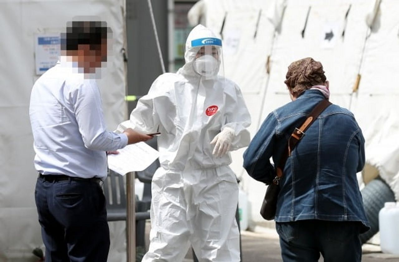 韓國街頭的COVID-19篩檢點，一位穿著防護服的工作人員正在協助民眾進行病毒檢測，展示當地抗疫工作的全面性。