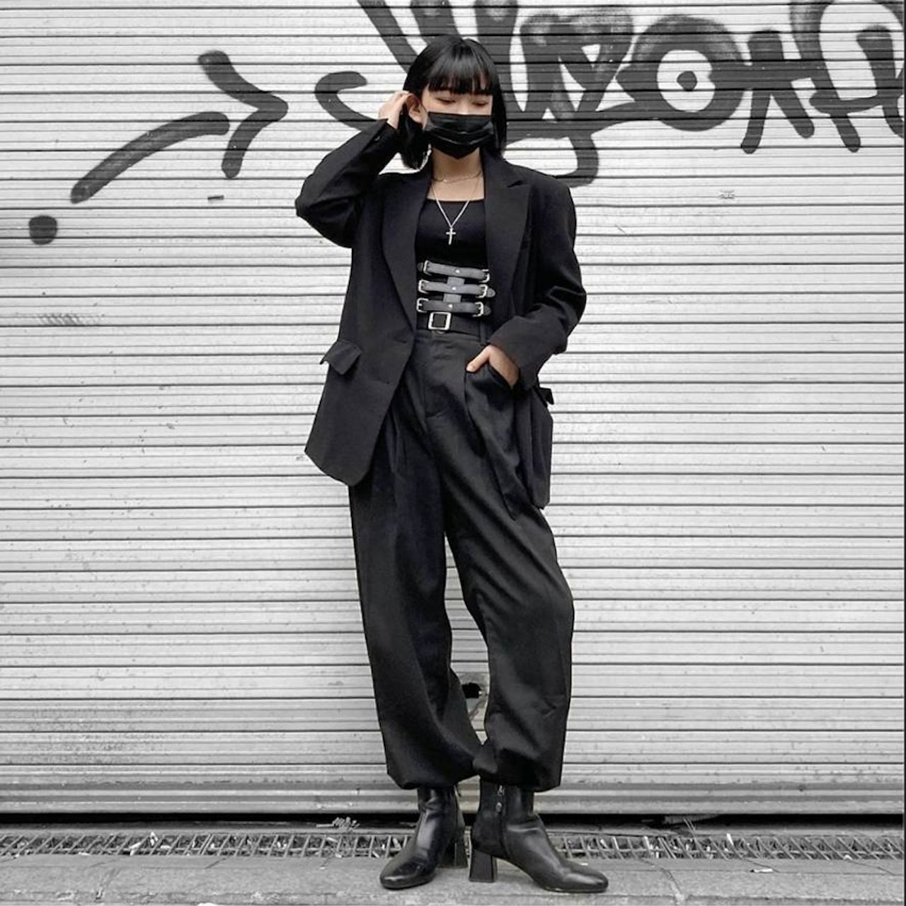 韓國黑暗系時尚裝扮，整體為黑色，搭配時尚飾品，背景是一面有塗鴉的鐵門。