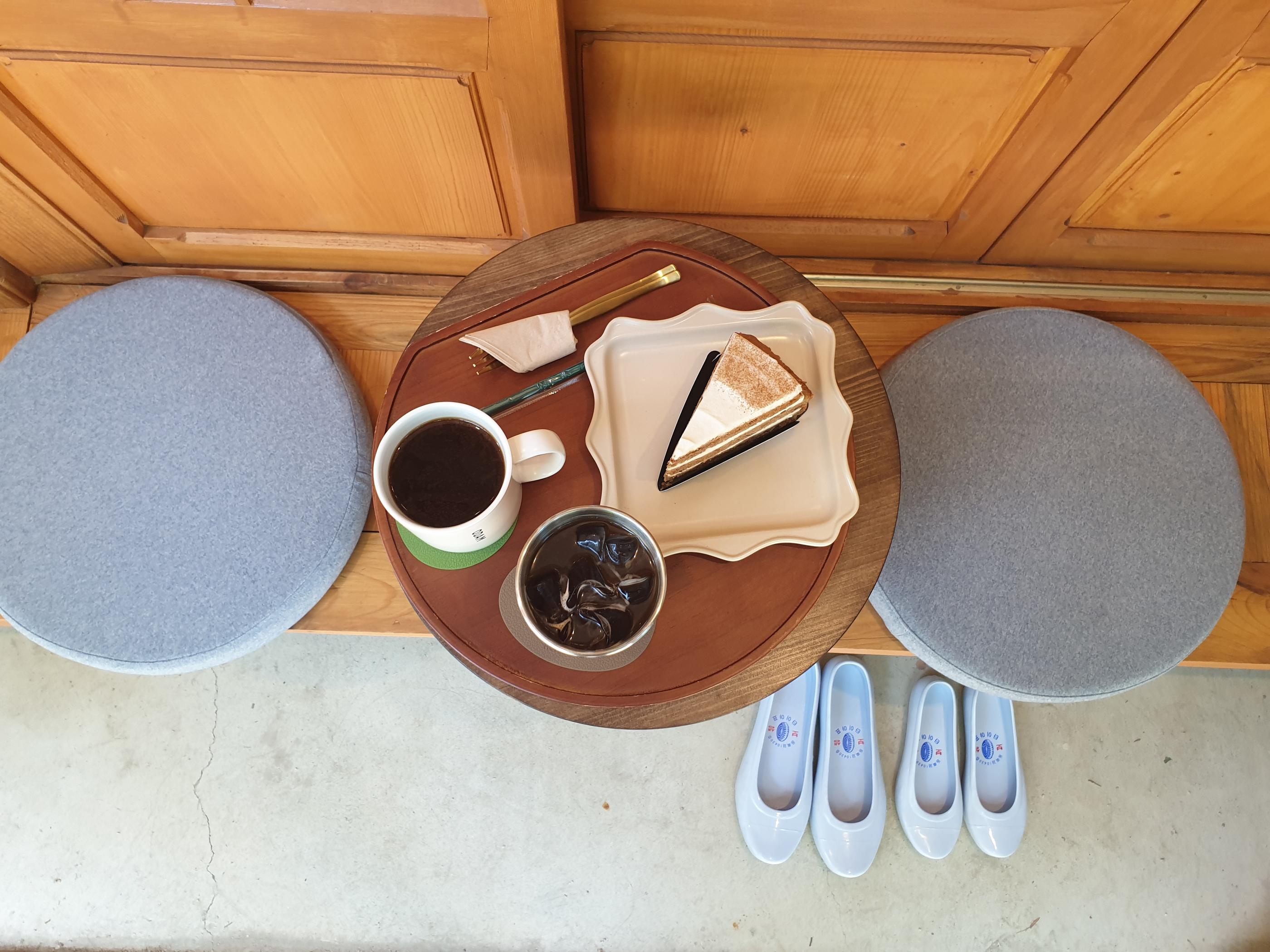 韓屋カフェの木製の座席スペースとベンチに置かれたドリンクとキャロットケーキが、歴史を感じる韓屋の雰囲気と調和。