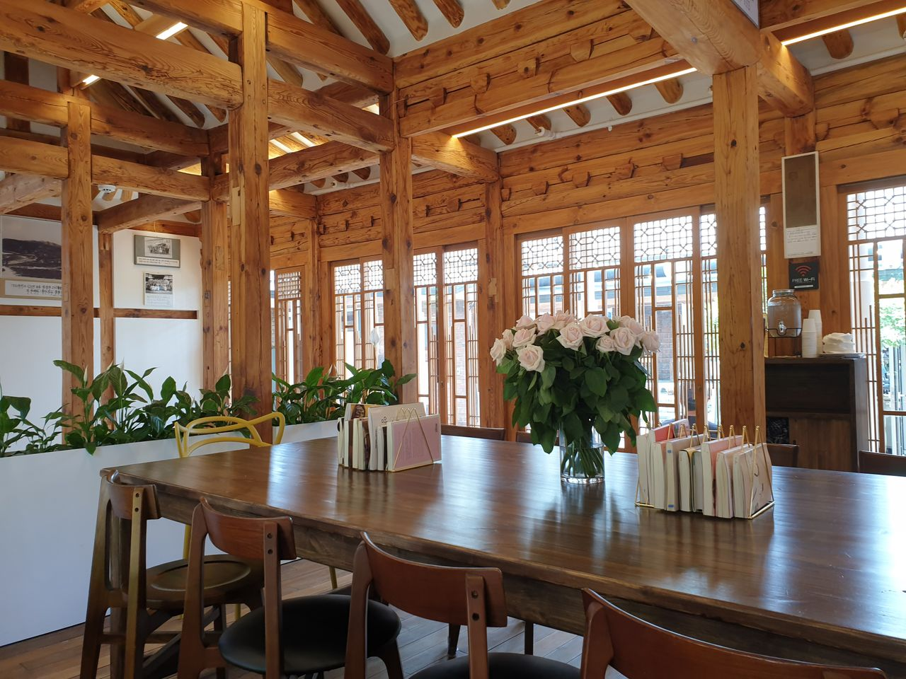 大きなダイニングテーブルとバラが飾られた、韓屋カフェの明るくオープンなインテリア。