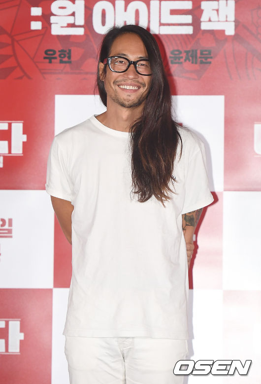 Persona in piedi di fronte a un fondale di un evento OSEN, vestita con una maglietta e pantaloni bianchi. L’immagine è stata modificata per oscurare il volto.