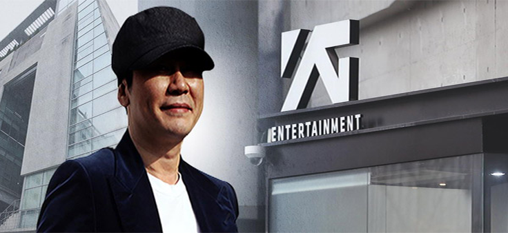 穿著帽子和西服的男士站在YG娛樂公司建築前，背景為現代辦公樓外觀。