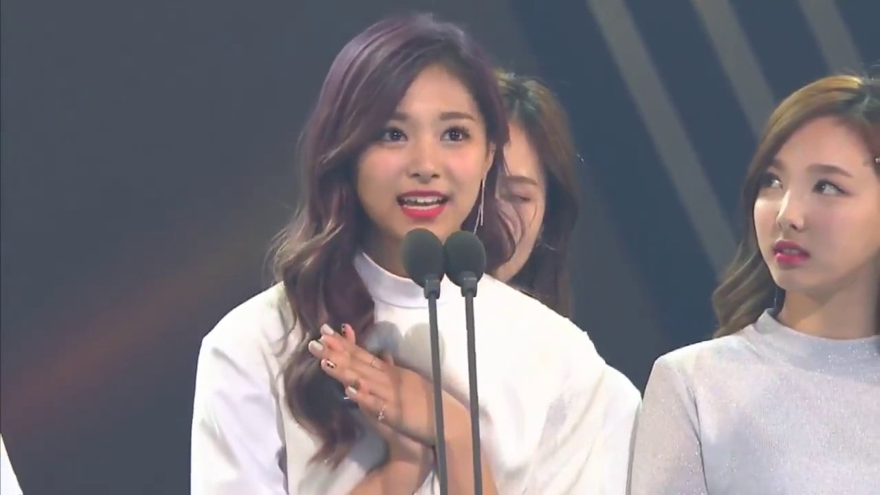 韩国女团在颁奖典礼上获奖发言，她们身穿时尚礼服，神情激动，象征着韩流文化的成功与影响力。