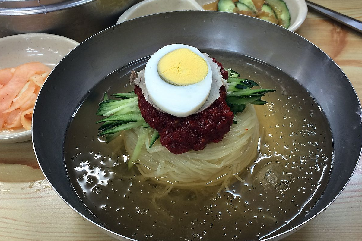 釜山特色小麥冷麵，上面放著半顆熟蛋、黃瓜絲與辣椒醬作為裝飾，清淡可口。