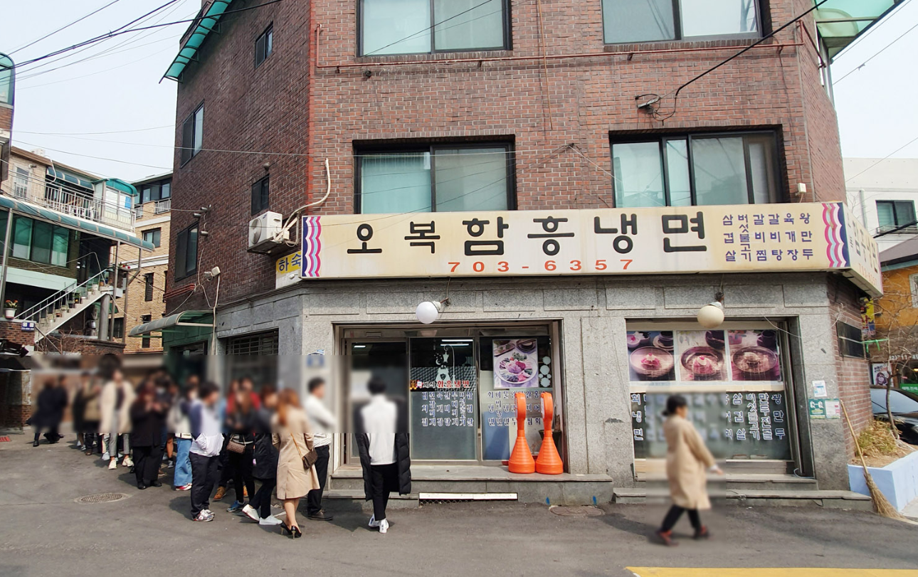 オボクハムン冷麺の外観写真。レンガ造りの建物で、店名が大きく看板に掲げられ、多くの人々が店前で並んでいる様子。