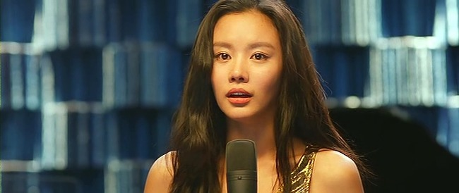 韓國電影《醜女大翻身》中,女主角站在麥克風前,一片藍色的背景突顯出她演唱時的自信與獨特魅力。