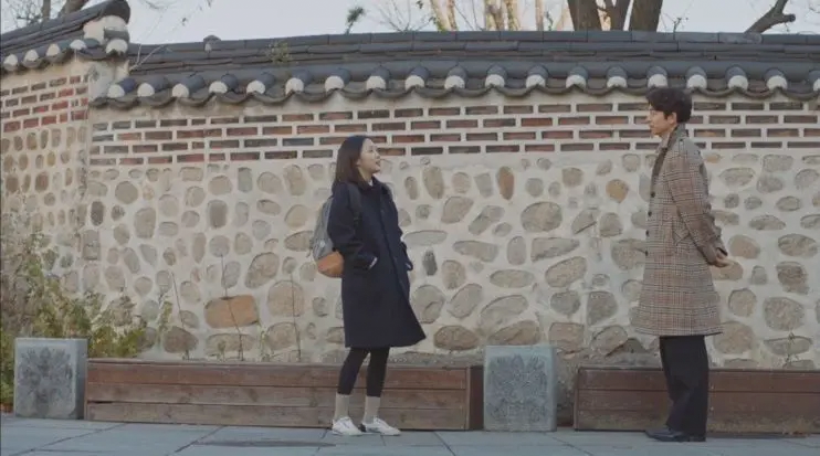 Goblin drama characters conversing in front of stone wall, Deoksugung Stonewall Walkway location.