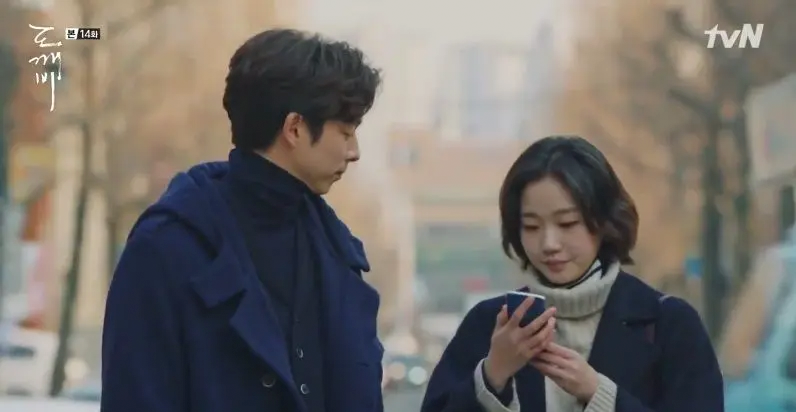 Two characters standing outdoors in Goblin drama scene, blurry urban background, Incheon Art Platform.