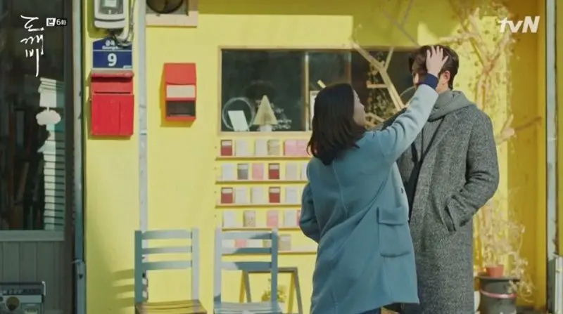 Hanmi Bookstore scene from Goblin drama with characters touching heads in front of yellow building.