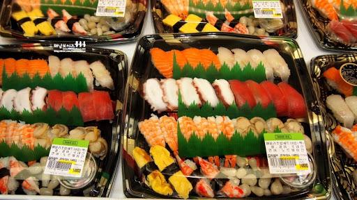 ถาดซูชิหลากหลายชนิดที่วางขายในซุปเปอร์มาร์เก็ต แสดงการวางเรียงอาหารสำเร็จรูปเพื่อการเก็บง่าย