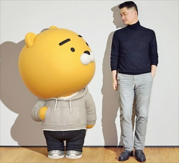 Kakao的吉祥物，Ryan，站在创始人旁边，象征公司形象。