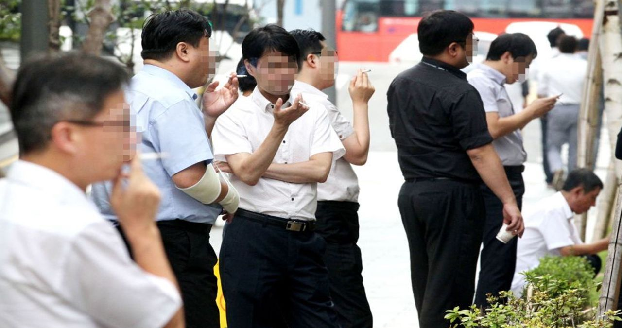 韓國都市街道上多位男士在吸煙區聚集，反映韓國社會中的抽煙現象。