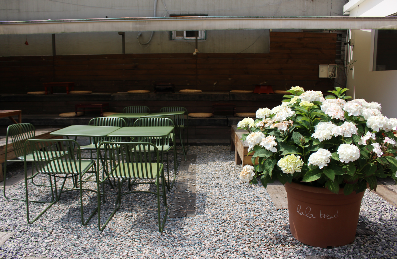 LALA BREADハンナム店の庭にあるテラス席。緑のガーデンチェアとテーブル、そして満開のアジサイの鉢植えが見える画像。