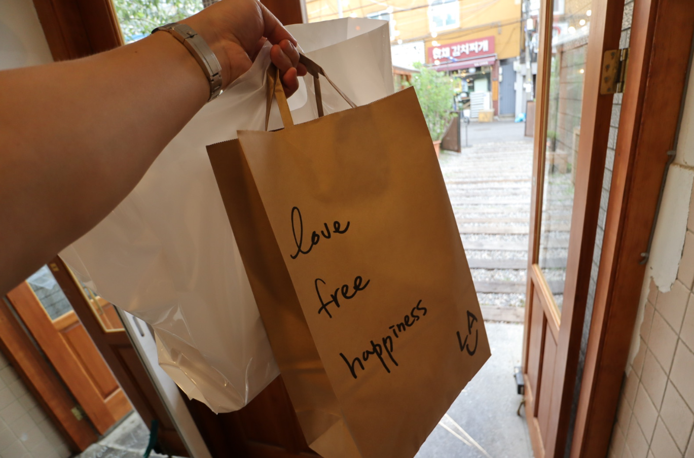 LALA BREADハンナム店から購入品を手に外へ出る場面。バッグには「Love free happiness」のメッセージがあります。
