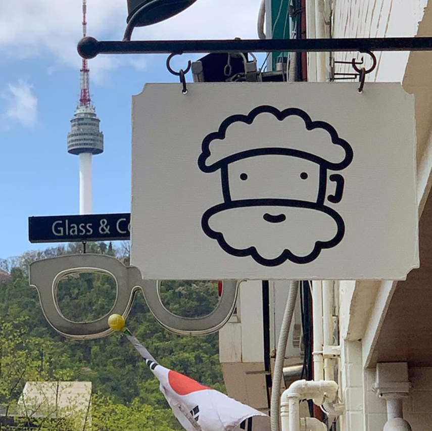 外に掲げられた白い看板には、かわいい泡キャラクターの絵が描かれており、背景には韓国の有名な南山タワーが見えます。忠武路にある人気カフェの外観です。