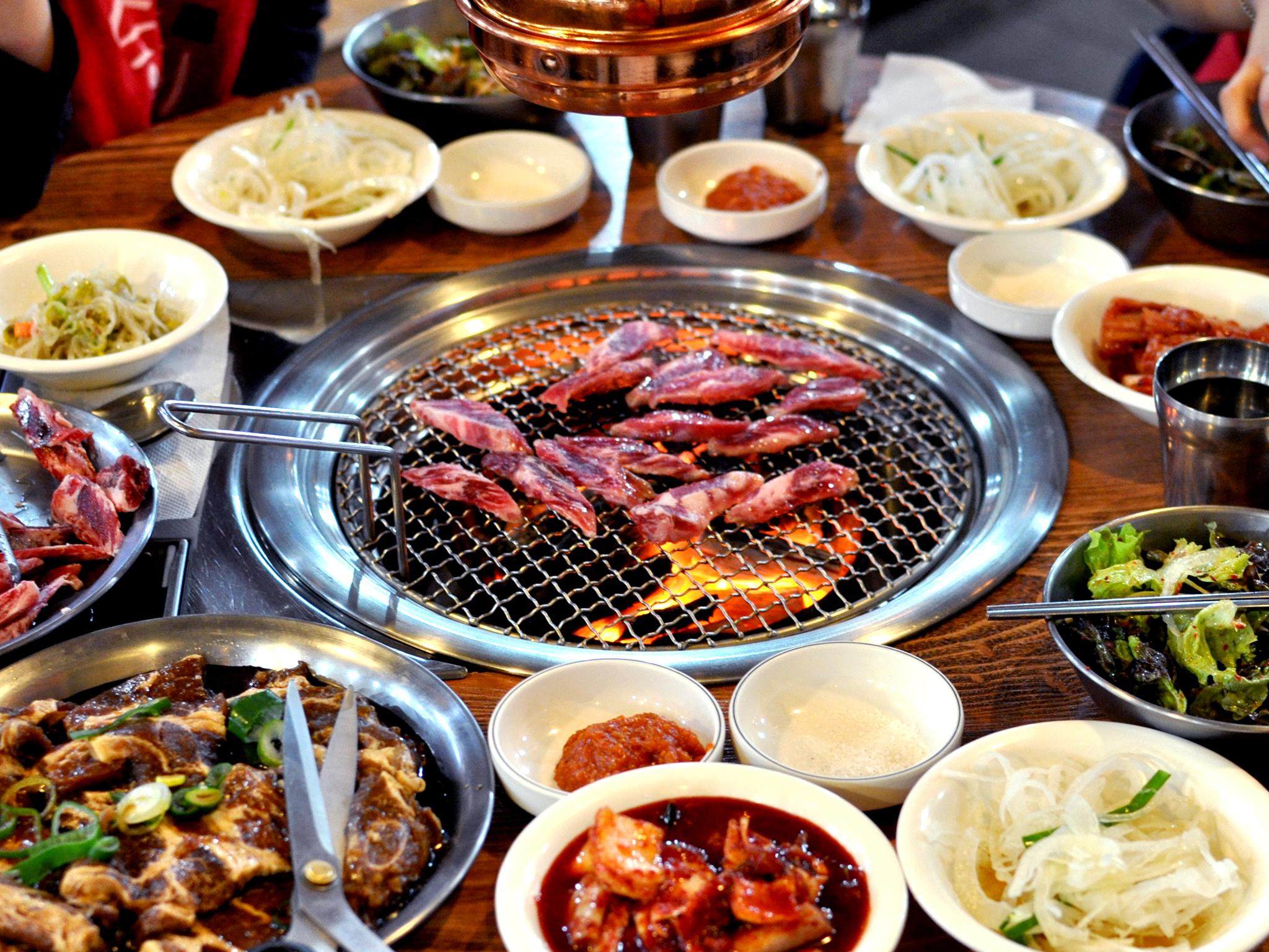บาร์บีคิวเกาหลีชั้นดีบนเตาถ่านร้อน พร้อมเนื้อและกิมจินานาชนิดบนโต๊ะอาหารที่มีเครื่องเคียงจัดเต็มตามแบบเกาหลีแท้ ๆ เหมาะสำหรับเพื่อนฝูงและครอบครัวที่ร่วมรับประทาน
