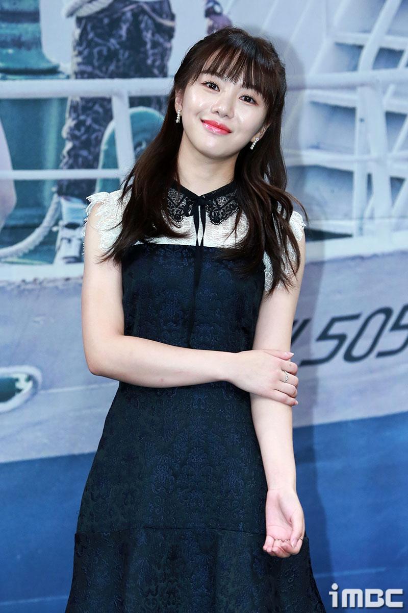 AOAジミンがAOAメンバークォン・ミナに謝罪する事件について、公式イベントで撮影された写真。背景にはブレザー姿の人物と船が見え、ジミンは黒いレースの襟付きドレスを着用している。