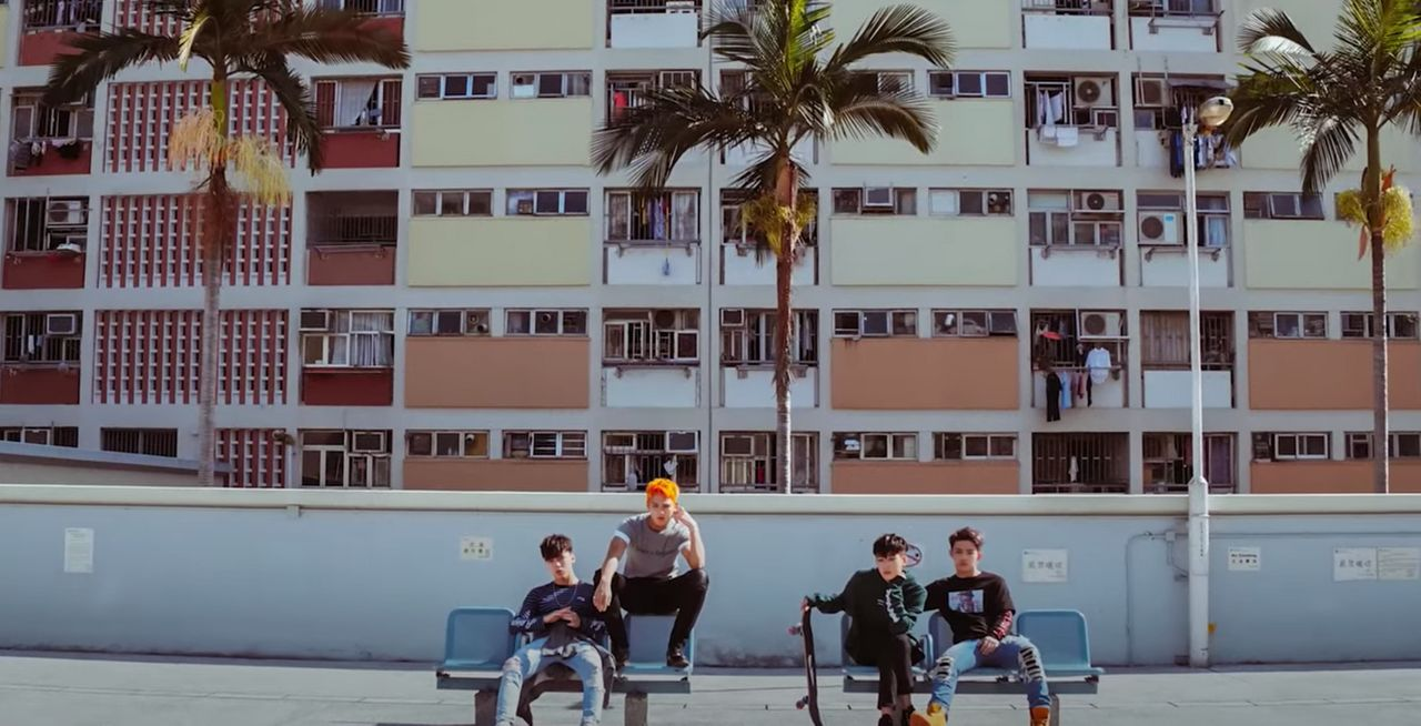 兩位穿著時尚的男星在香港的一個特色公共屋邨前面拍照，這裡是一個吸引韓國明星的拍攝熱點。