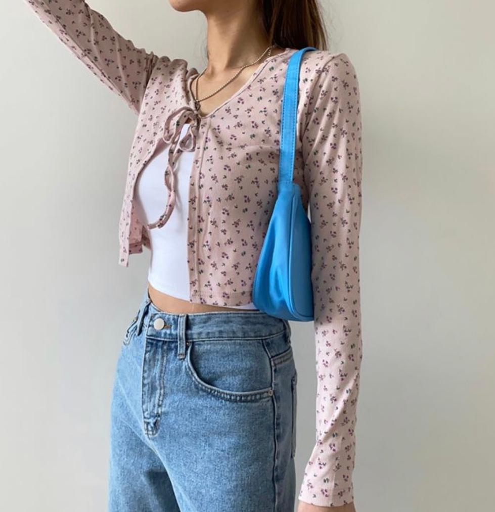 ピンクの花柄トップスと青のデニムパンツを履いた女性。青いショルダーバッグを肩にかけている。