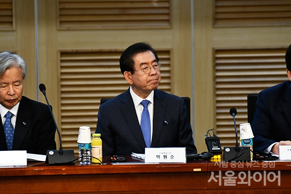 韩国首尔市政府会议场景，桌上摆放着会议材料和饮料杯，图像中的会议参与者坐在会议桌旁，其中一位穿着西装打着领带，展示了正式场合的会议情境。