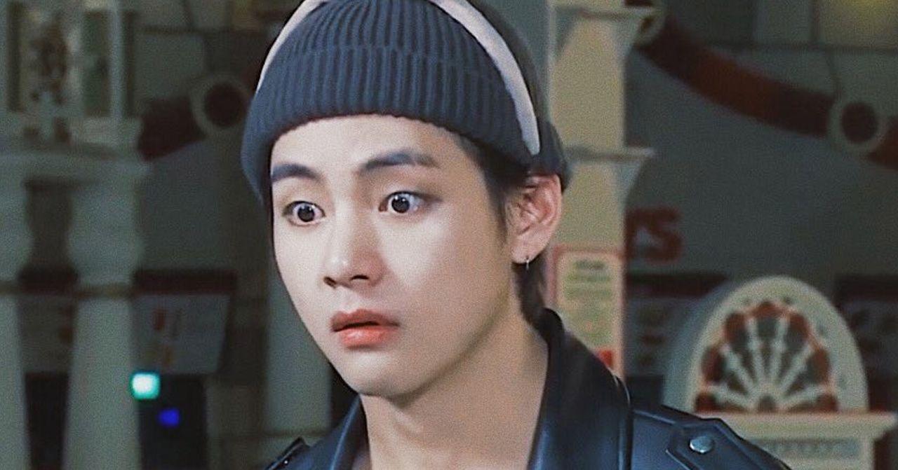 ชายสวมหมวกสีเทาและเสื้อแจ็คเก็ตหนังยืนอยู่ในสวนสนุกเกาหลี ด้วยบรรยากาศที่เต็มไปด้วยสีสันจากอาคารและแสงไฟต่าง ๆ 