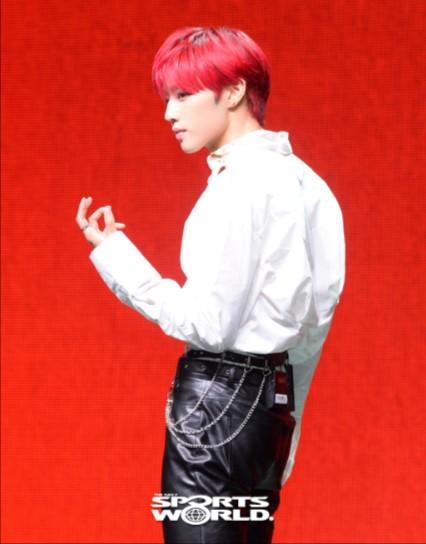 THE BOYZのメンバーが白いシャツと黒いパンツを着て、赤い背景の前でポーズをとっている。