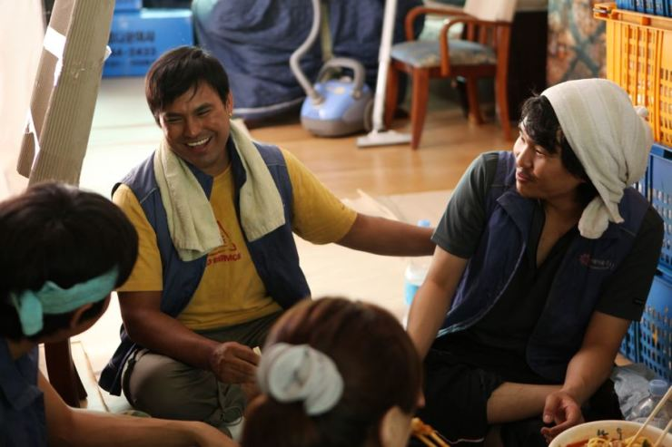 ภาพแสดงกลุ่มแรงงาน กำลังรวมตัวกันเพื่อสนทนาในที่พักหลังเลิกงานที่ประเทศเกาหลีใต้ ซึ่งสะท้อนชีวิตประจำวันของแรงงานต่างชาติในเกาหลี