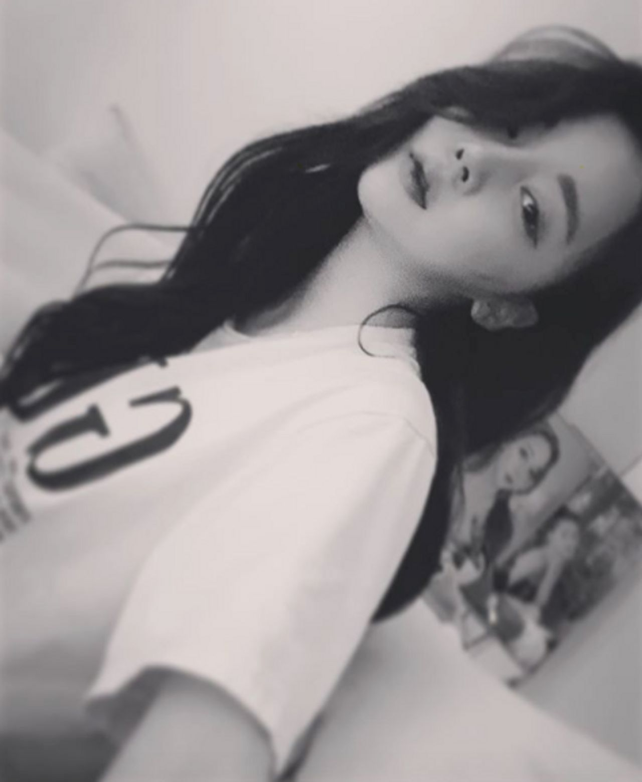 身穿印有字母T恤的女性自拍，背景中有一張粉絲簽名會的照片。