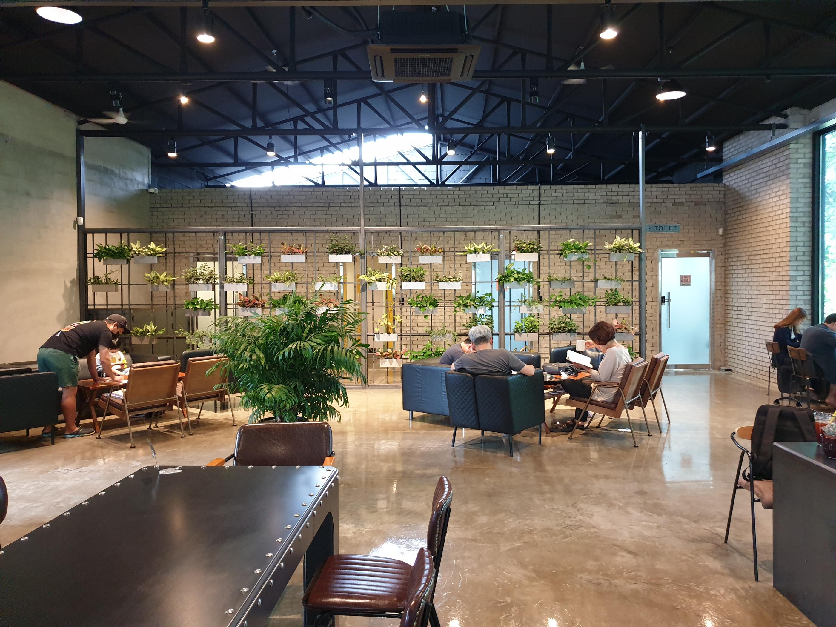 多くの座席と装飾植物が置かれたカフェの端的ビュー