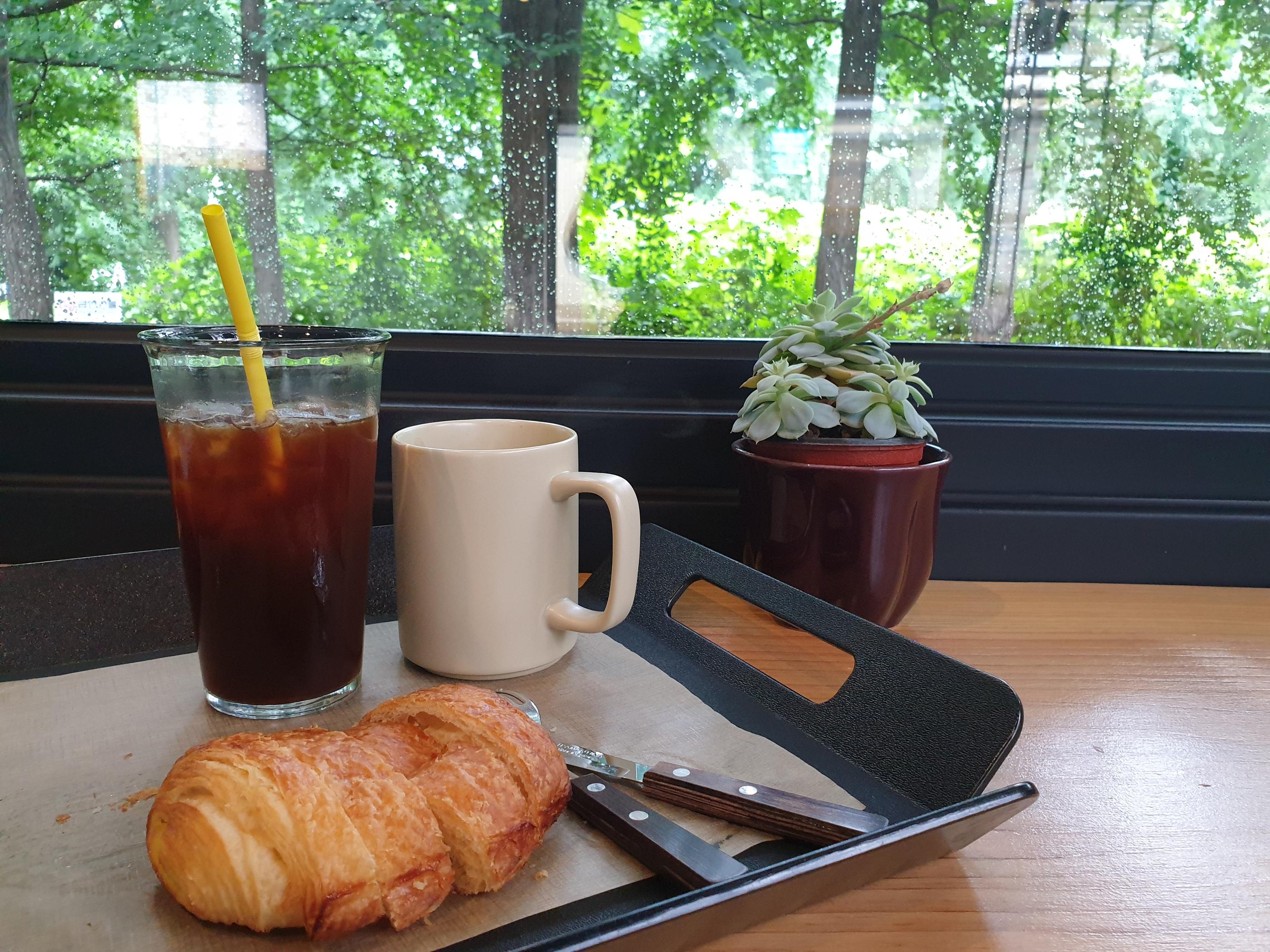 窓際のテーブルに置かれたアイスコーヒーとクロワッサンのセット