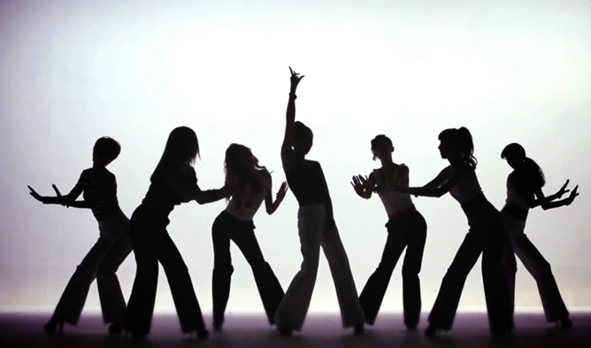 เงาของกลุ่มคนที่กำลังแสดงท่าทางการเต้นโดยประสานกัน บนพื้นหลังที่มีแสงสว่าง ซึ่งสะท้อนถึงศิลปินฟรีแลนซ์และผู้ประกอบอาชีพอิสระในการแสดง