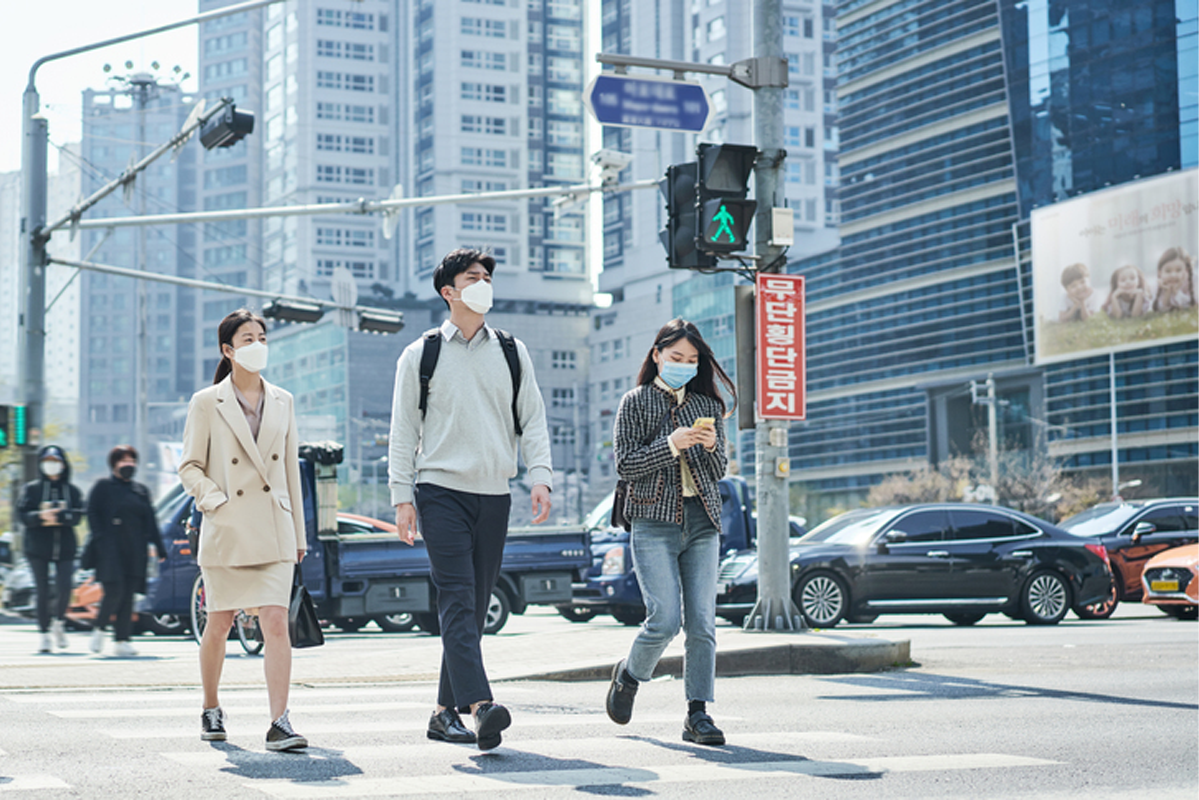 人們在斑馬線上快速行走，背景是現代高樓，展示了韓國城市生活的速度。