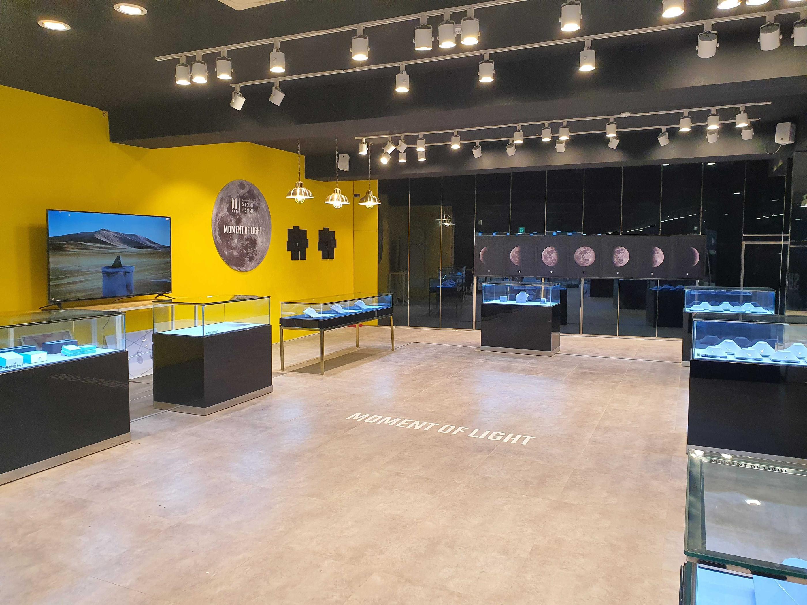 BTSとSTONE HENGEのコラボショップの内部ビュー。ディスプレイケース内に展示されたネックレスが目を引く。壁には月のフェーズを表現した装飾が飾られ、店内に幻想的な雰囲気を醸し出している。