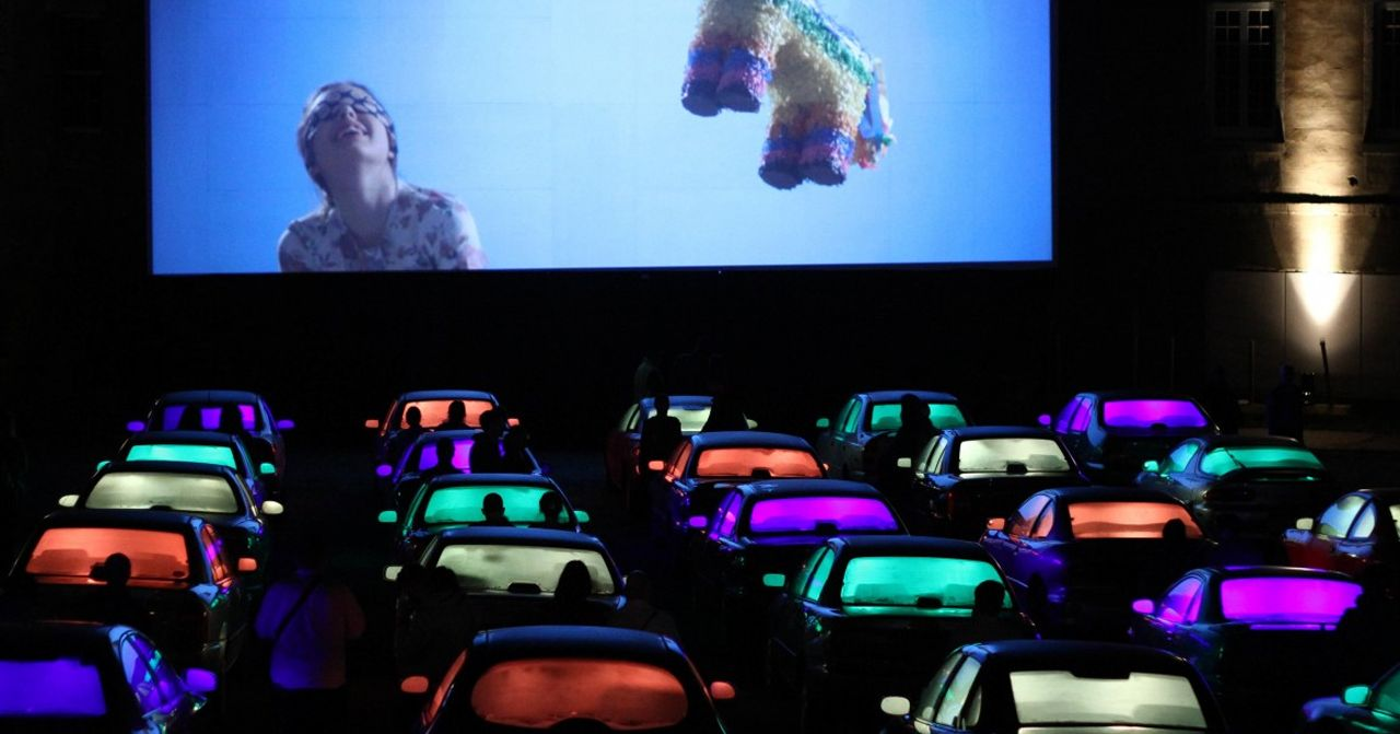 韓國CGV汽車戲院的場景，背景是一個正在播放影片的大螢幕，許多色彩斑斕的車輛停泊在螢幕前方，營造出全新的觀影體驗。