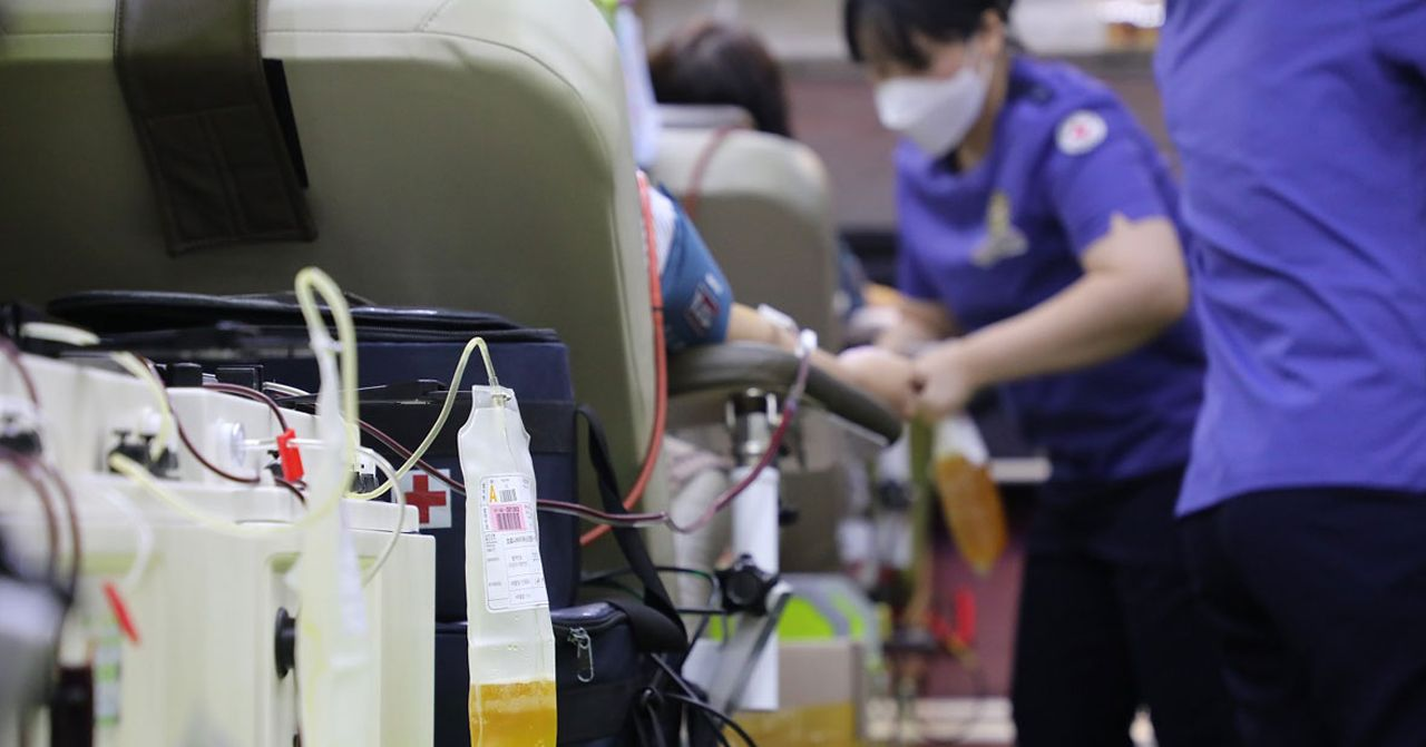 捐血活動現場，展示一個血袋正在進行輸血程序，背景中工作人員和捐血者出現，描繪出捐血的即時情況。