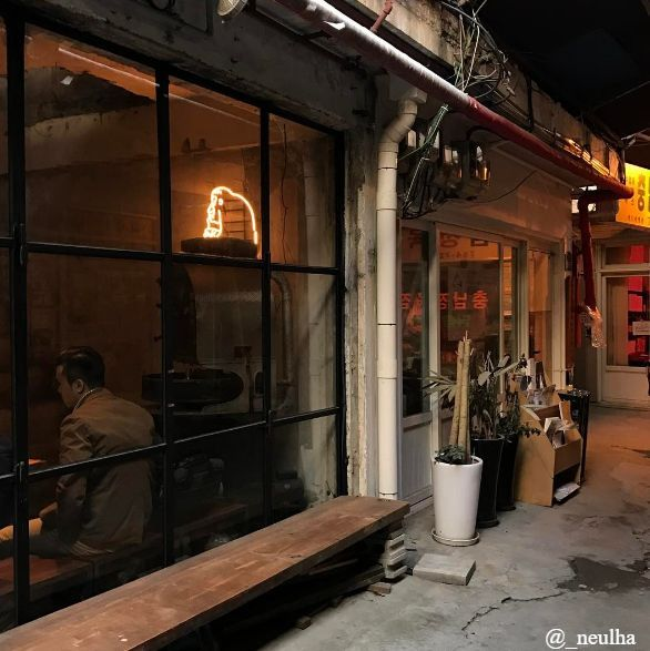 Một ly cà phê lạnh với ống hút, hậu cảnh là N Seoul Tower và bầu trời xanh sáng.