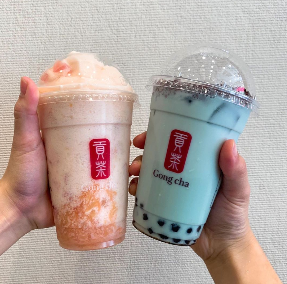 ゴンチャのミントチョコチップミルクティーとグレープフルーツヨーグルトクラッシュを手で持ち、明確な背景に映し出された画像。爽やかなミントカラーとフルーティーなグレープフルーツが特徴の新メニューを示している。