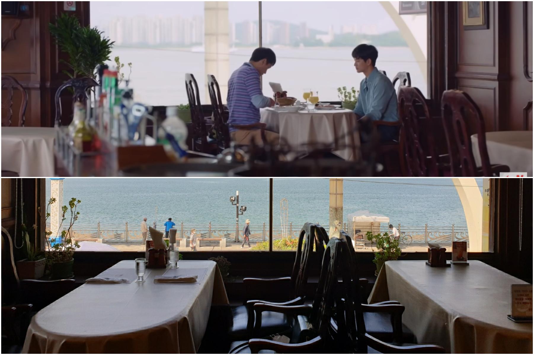 ドラマのシーンを思わせるレストランの内装と窓の外に広がる美しい海の景色。クラシックな木製の椅子とテーブルが置かれ、隣接する静かな風景が感じられます。