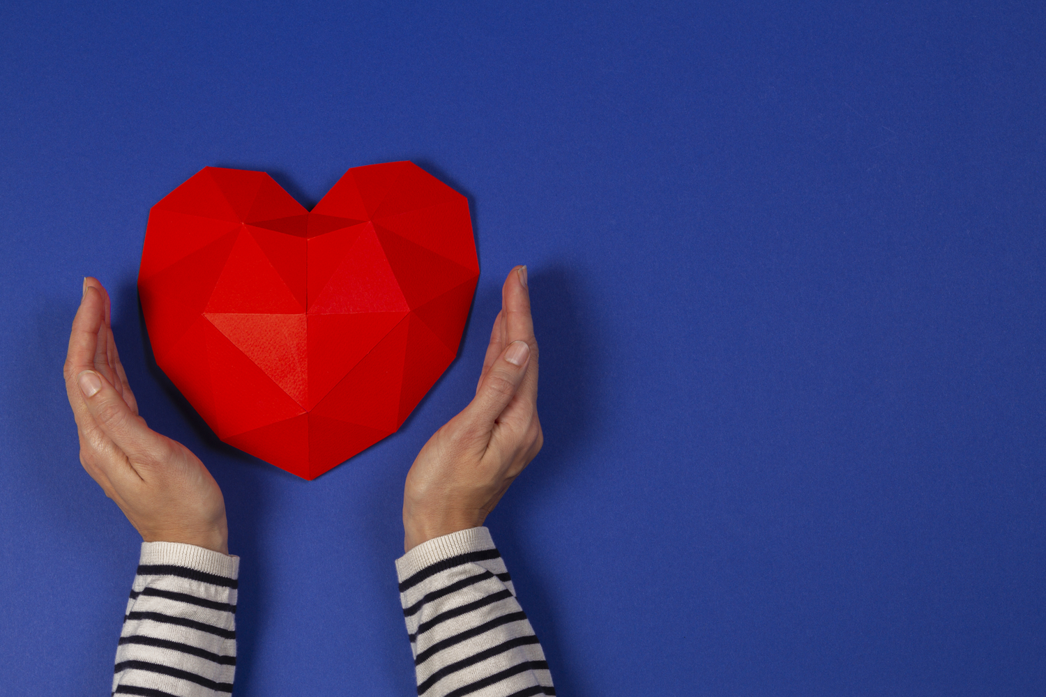 一雙手環抱著一個紅色的紙心形，象徵著愛與珍惜的關係。