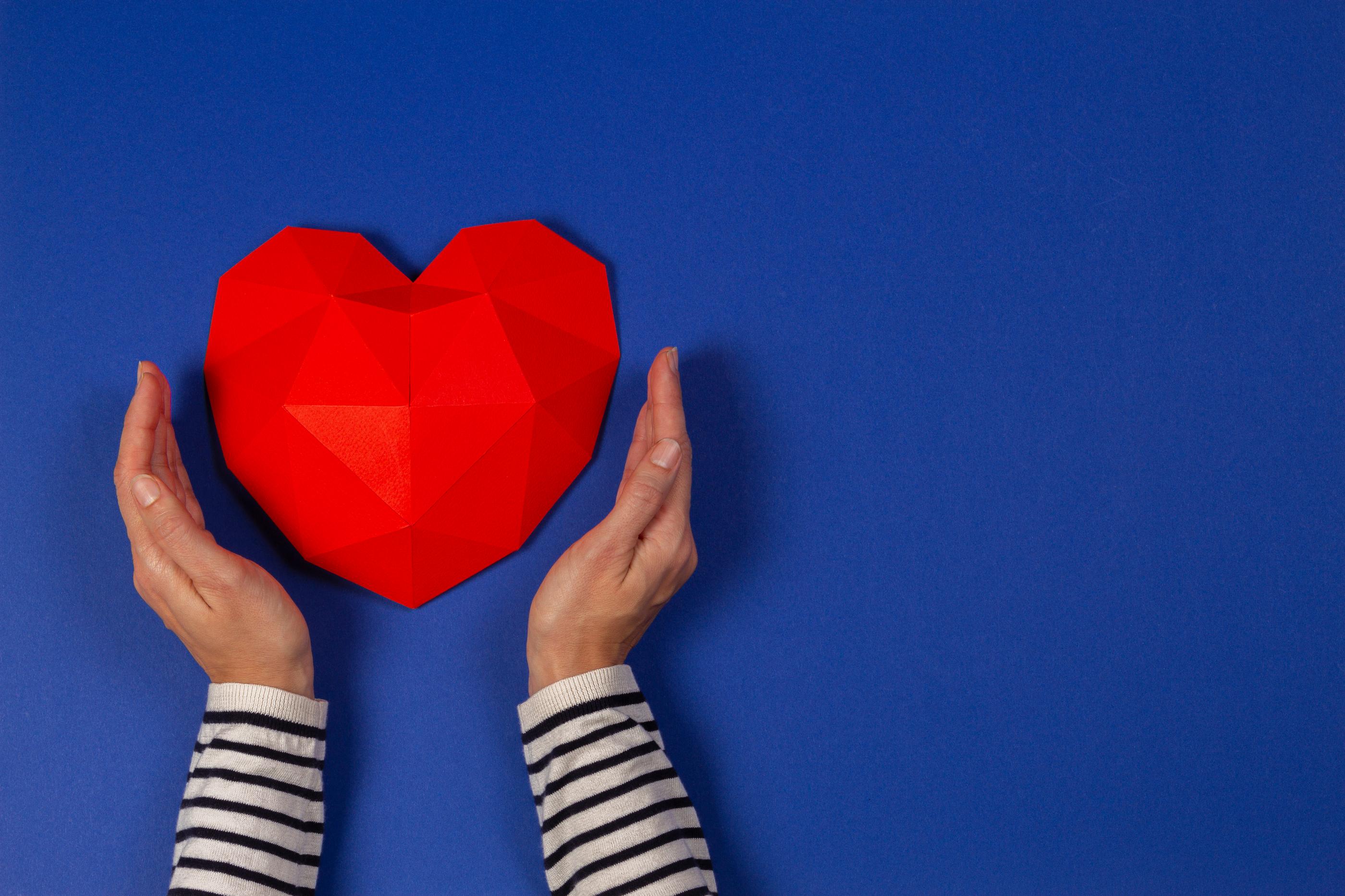 Tình yêu quân nhân: Đôi bàn tay nâng niu một trái tim đỏ giữa nền xanh, biểu tượng cho sự kiên trì và tình yêu bền chặt khi hẹn hò với một quân nhân Hàn Quốc.