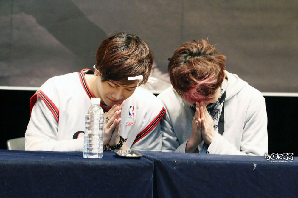 ชายหนุ่มสองคนซึ่งไว้มือตรงหน้าในท่าทางคล้ายสำนึกผิดระหว่างพูดคุยกันในงานแฟนมีตติ้ง