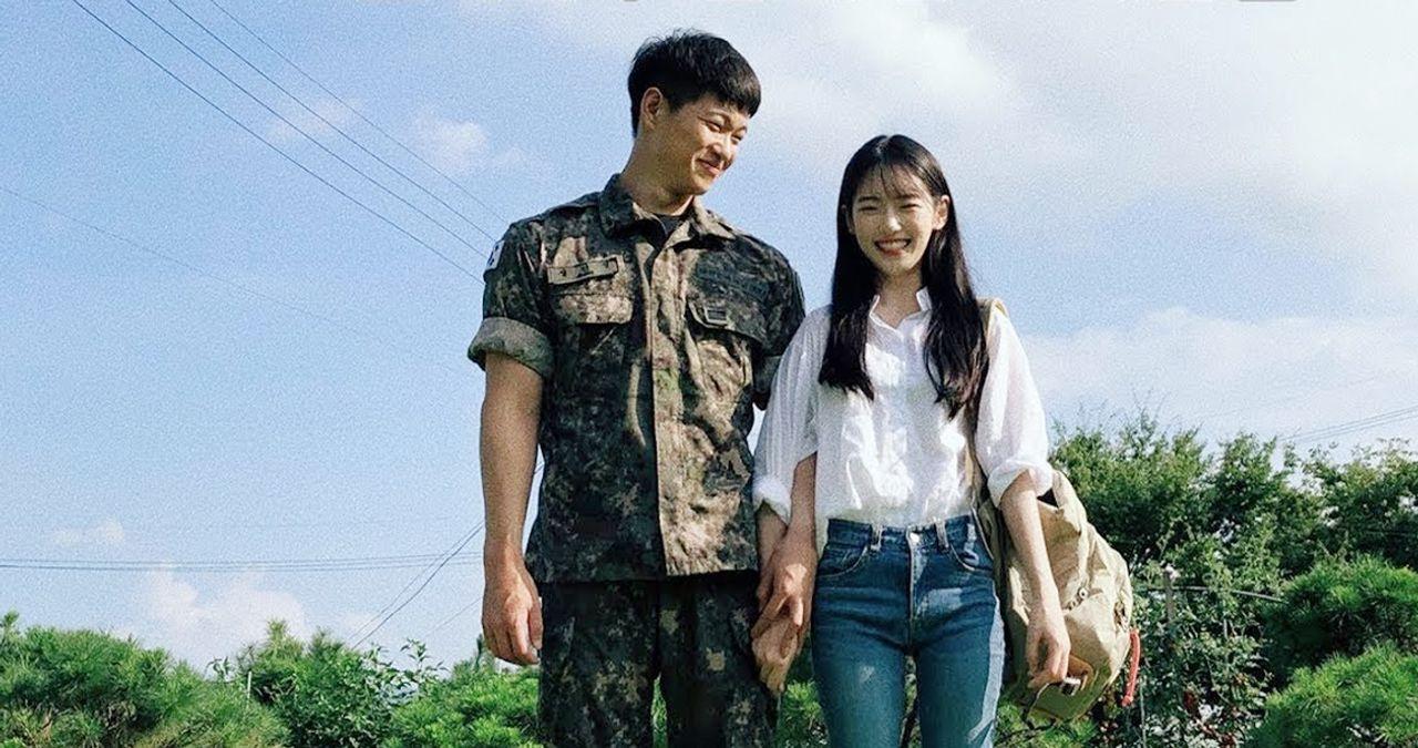 ชายในชุดทหารและหญิงสาวยืนจับมือกันบนถนนกลางวัน ข้อดีของการมีแฟนเป็นทหารเกาหลีคู่รักในบรรยากาศธรรมชาติ