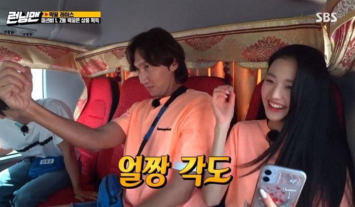 在韓國綜藝節目《Running Man》中，李光洙和張員瑛正在大巴上自拍，氣氛輕鬆愉快，兩人都穿著橘色T恤。