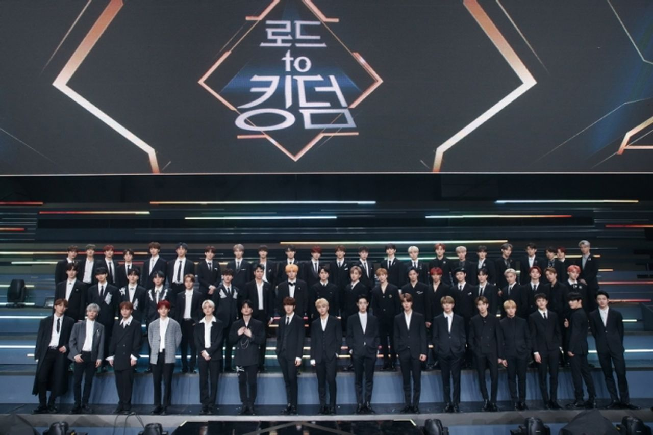 《Road to Kingdom》節目中的參加者們穿著正式西裝站在大舞臺上,背景中顯示出節目名稱。