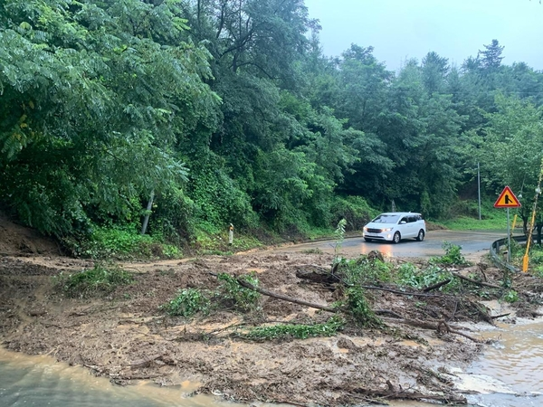 公路被大雨引發的滑坡堵住，一輛白色汽車小心駛過濕滑的道路。