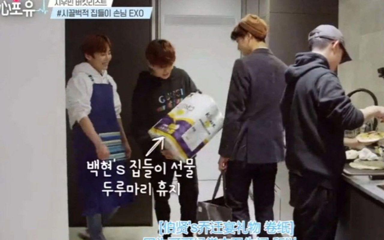 ภาพคนสวมผ้ากันเปื้อนและเพื่อนร่วมกลุ่มที่กำลังถือแพ็กกระดาษ ในบรรยากาศที่แสดงการมอบของขวัญหรือการเยี่ยมเยียน