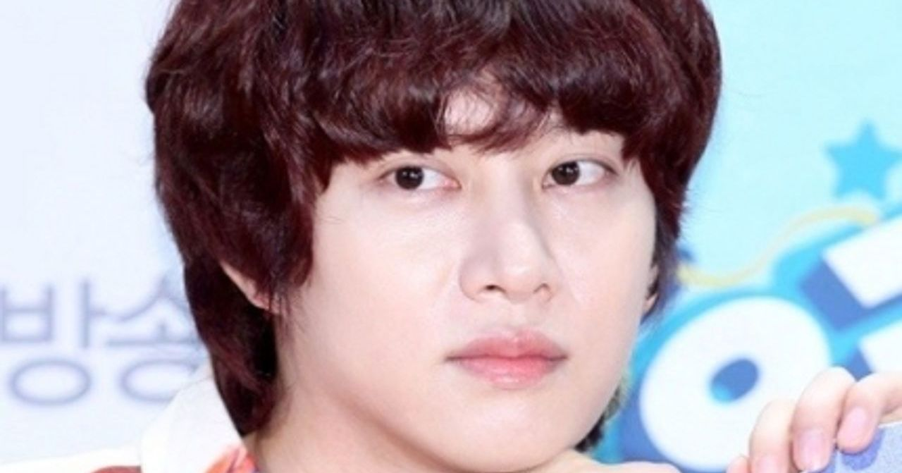 韓國偶像藝人希澈，擁有紅色短髮，穿著印有花卉圖案的休閒裝，背景是一個以藍色為主色調的舞臺。