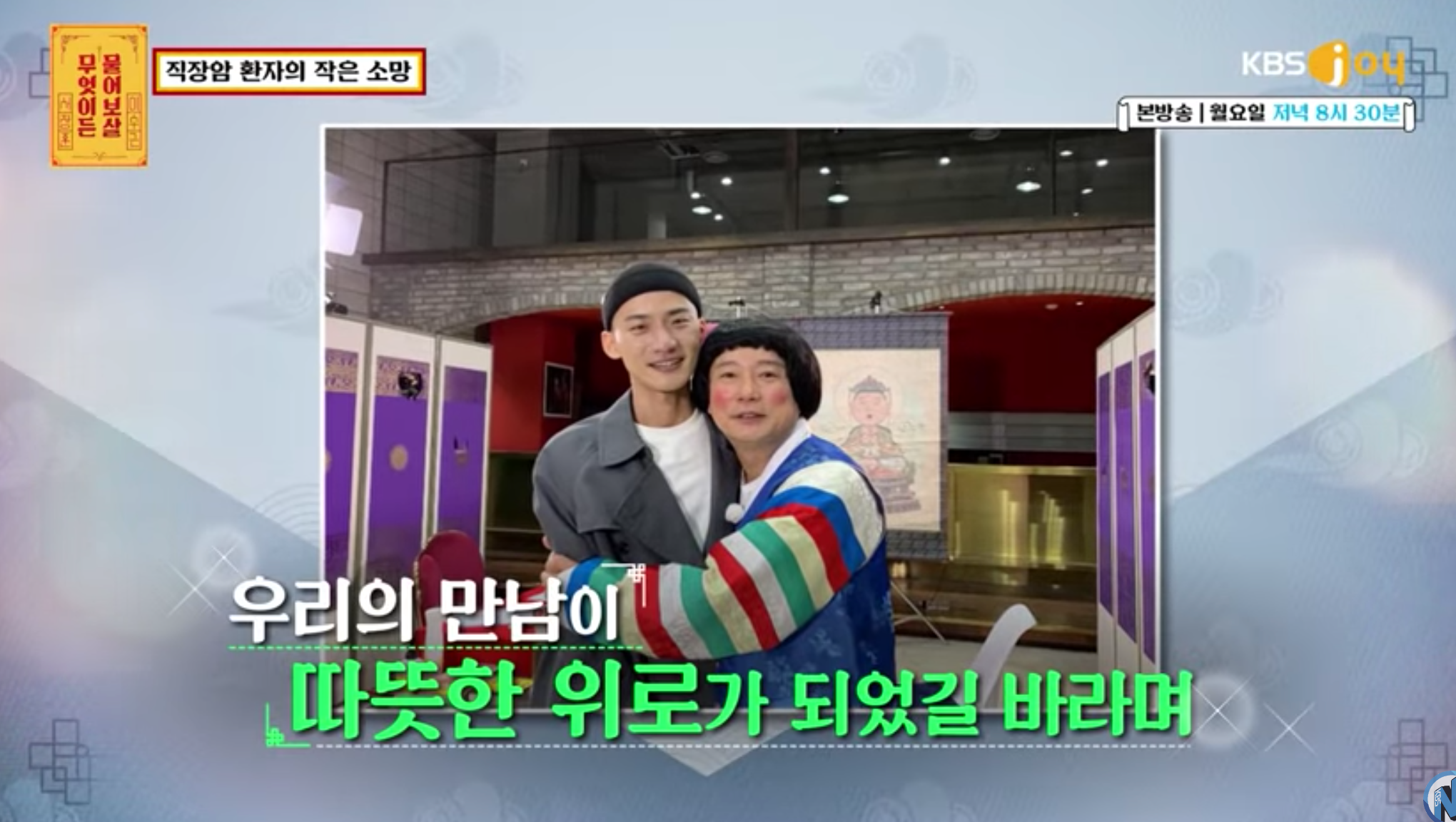 韓國電視節目中的一對男子合影,背景有識別性韓國標誌和圖像佈置