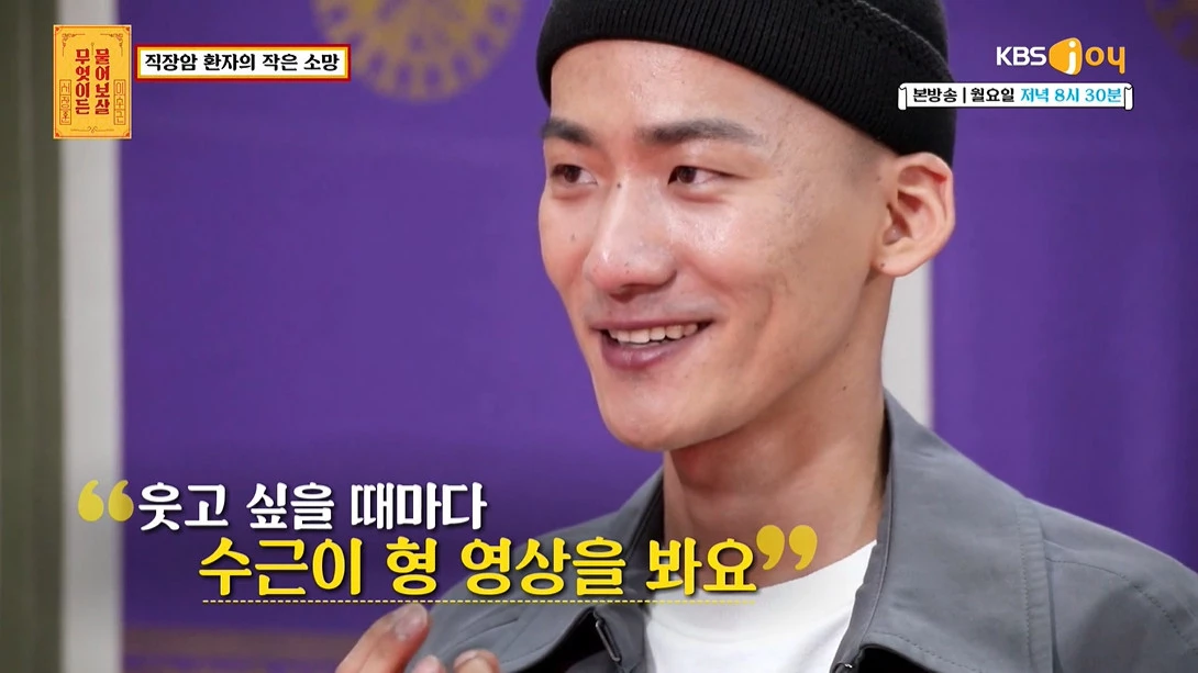 一名男子在舞臺上唱歌,背景中有大型紫色掛布和燈光設置