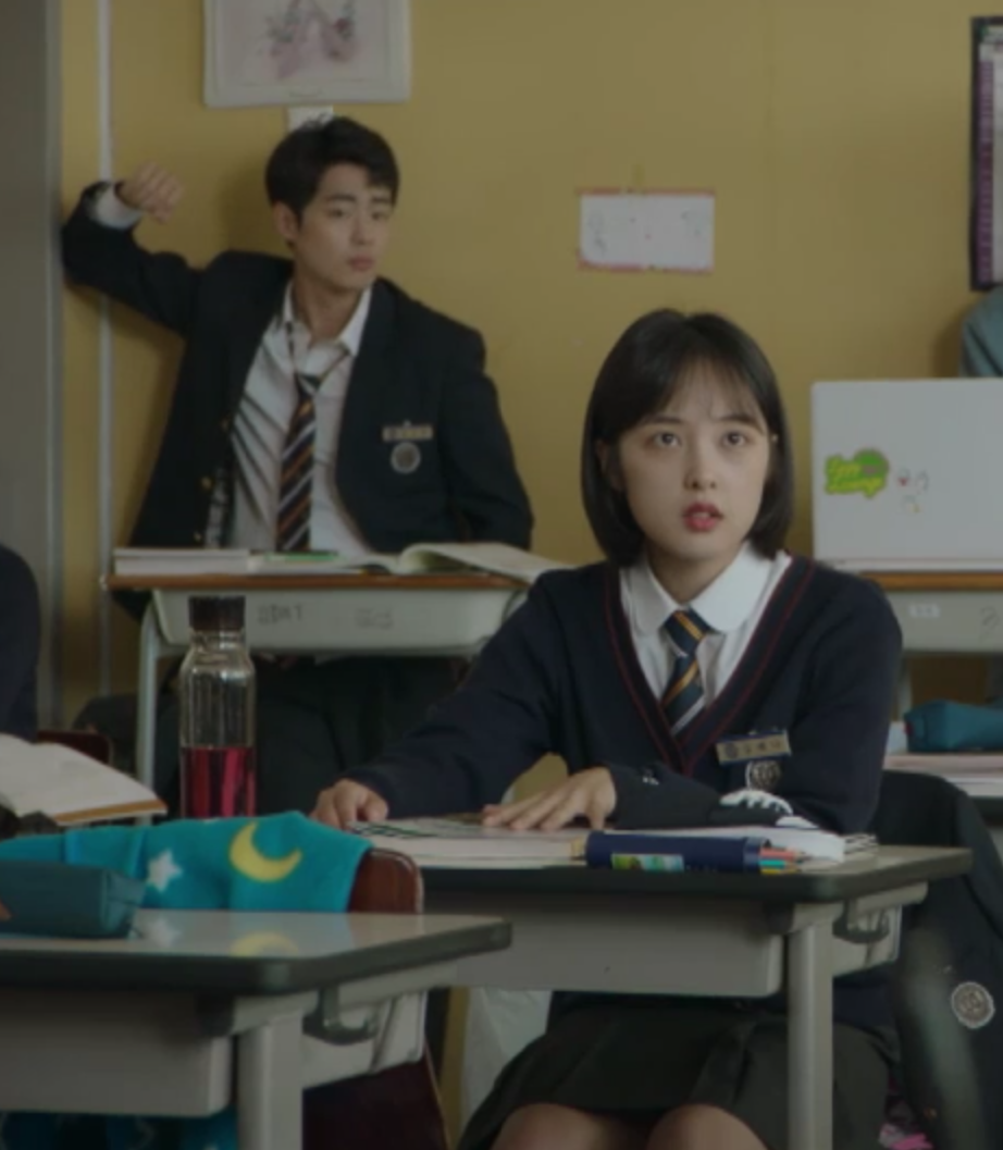 韓劇《天空之城》中學生穿著校服坐在教室，前景為一名女學生，後方有一名學生靠在牆邊。
